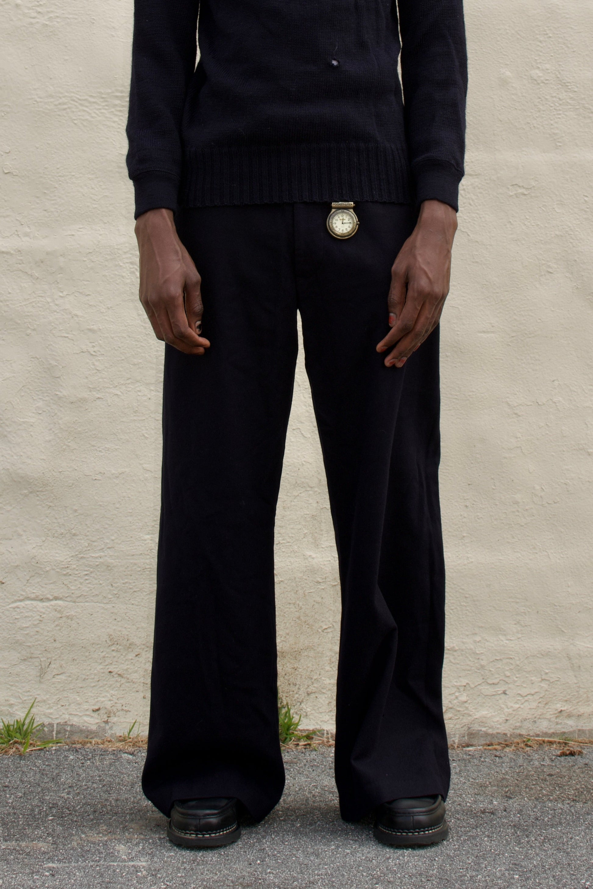 Person wearing a black turtleneck and pants standing against a plain wall.